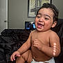 arm, baby, bed, black_bedspread, bridge_art, candid, child, diaper, door, face, hair, hand, happy, indoor, laughing, leg, picture_frame, skin, smiling, wall