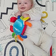 Gabriel a rejoint le concours — aidez-le/la à gagner de superbes lots ! baby, infant, smiling, toy, plush_toy, onesie, playmat, lying_down, cute, happy, cheeks, hand, feet, blond_hair, portrait, indoor, patterned_background, colorful, baby_toy, relaxed