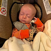 Carter joined the competition — help win amazing prizes! baby, infant, sleeping, car_seat, blanket, mitten, sweater, orange, striped_clothing, cozy, portrait, face, closed_eyes, indoors, vehicle, safety_label, cuddled, newborn, resting, photograph