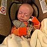baby, infant, sleeping, car_seat, blanket, mitten, sweater, orange, striped_clothing, cozy, portrait, face, closed_eyes, indoors, vehicle, safety_label, cuddled, newborn, resting, photograph