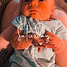 baby, clothing, cute, expression, face, hands, holding, human, indoor, infant, newborn, pajamas, person, relaxation, sitting, skin, tattoo, text_overlay, warm_light, weekend
