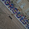 architecture, building, cobblestone, colorful_letters, daylight, dog, flower_pattern, leash, no_people, outdoor, pavement, public_space, quiet, shutters, sidewalk, sign, small_dog, street, urban, vintage_style