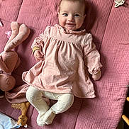 Julia a rejoint le concours — aidez-le/la à gagner de superbes lots ! baby, pink_dress, tights, smiling, face, soft_toys, pacifier, blanket, child, infant, cute, lying_down, indoors, happy, playful, cozy, person, fabric, toy, portrait