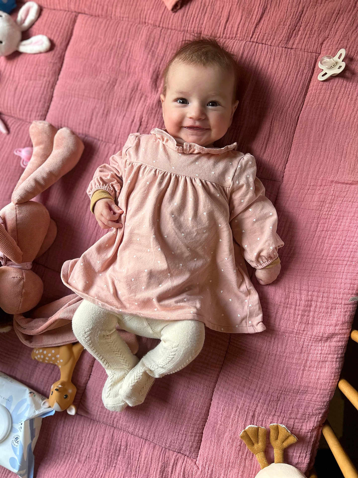 Julia a rejoint le concours — aidez-le/la à gagner de superbes lots ! baby, pink_dress, tights, smiling, face, soft_toys, pacifier, blanket, child, infant, cute, lying_down, indoors, happy, playful, cozy, person, fabric, toy, portrait