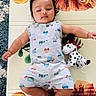 baby, infant, child, play_mat, lion_design, plush_toy, spotted_dog, grey_outfit, vehicles_print, indoor, carpet, cute, lying_down, calm_expression, black_hair, soft_lighting, colorful, toy, childhood, floor
