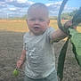 blue_shoes, casual_clothing, child, clouds, curious, daylight, field, fruit, grass, green, leaf, nature, outdoor, portrait, shorts, sky, standing, summer, toddler, tshirt
