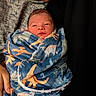 newborn, baby, infant, child, face, portrait, swaddled, blanket, dinosaur_pattern, adult, parent, cuddling, indoor, close_up, sleepy, alert, skin, nose_piercing, textile, family