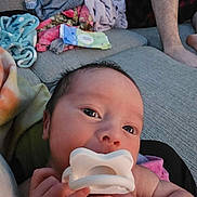 Roman is registered to the contest to win money with this photo: baby, infant, child, pacifier, portrait, close_up, face, eyes, hands, smiling, indoor, home, sofa, blanket, clothing, adult, family, cozy, sitting, photography