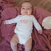 Lila a rejoint le concours — aidez-le/la à gagner de superbes lots ! baby, infant, blanket, floor, wooden_floor, onesie, butterfly, plaque, milestone, pink, white_clothing, cute, lying_down, chubby, young_child, smiling, indoors, soft_texture, milestone_marker, portrait