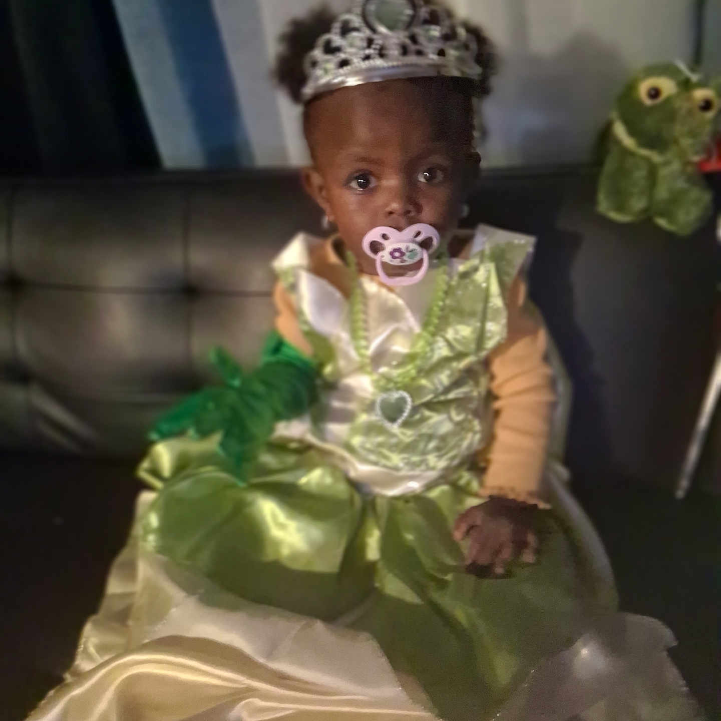 Reijanae is registered to the contest to win money with this photo: baby, child, costume, couch, curious, cute, dress, frog, gloves, green_dress, indoor, jewelry, necklace, pacifier, portrait, sitting, stuffed_animal, tiara, toy, young