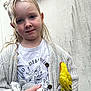 child, blonde_hair, curly_hair, blue_eyes, knitted_cardigan, white_shirt, floral_print, plush_toy, yellow_bird, bird_perched, hand_holding, outdoor, wall_background, portrait, smile, cute, young, cozy, gentle, calm