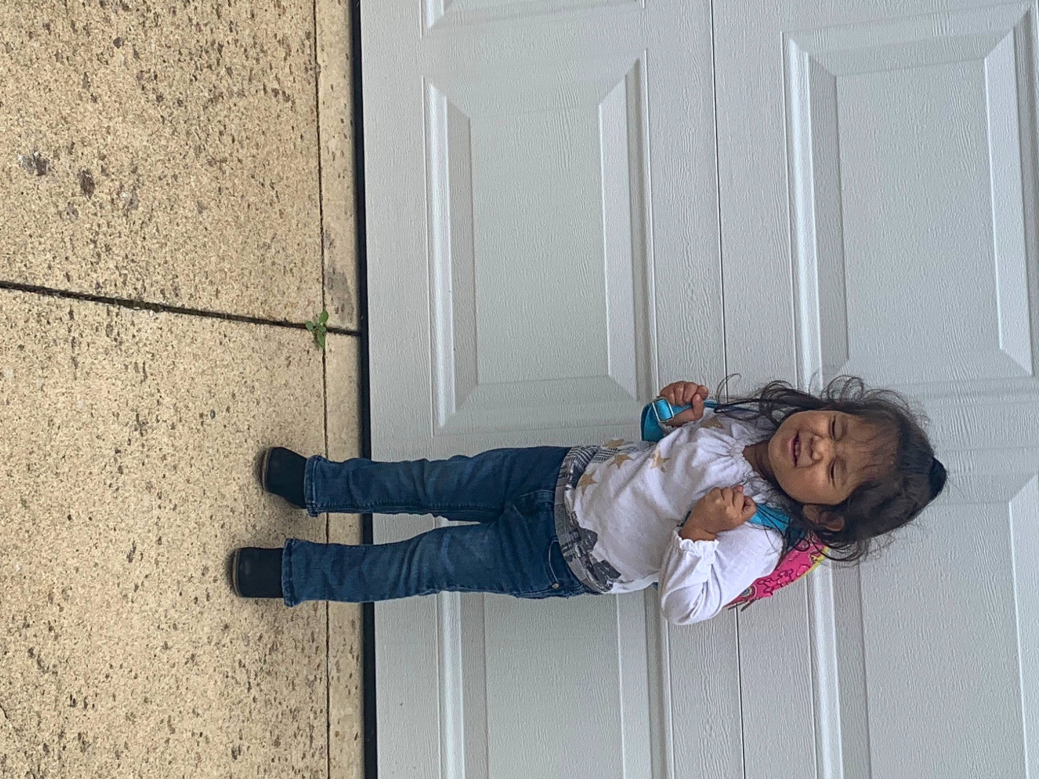 Mariana is registered to the contest to win money with this photo: concrete, denim, electric_blue, facade, flooring, human_leg, line, pedestrian, person, road_surface, shadow, shoe, sidewalk, sitting, street, sunglasses, toddler, tree, walking_shoe, wall