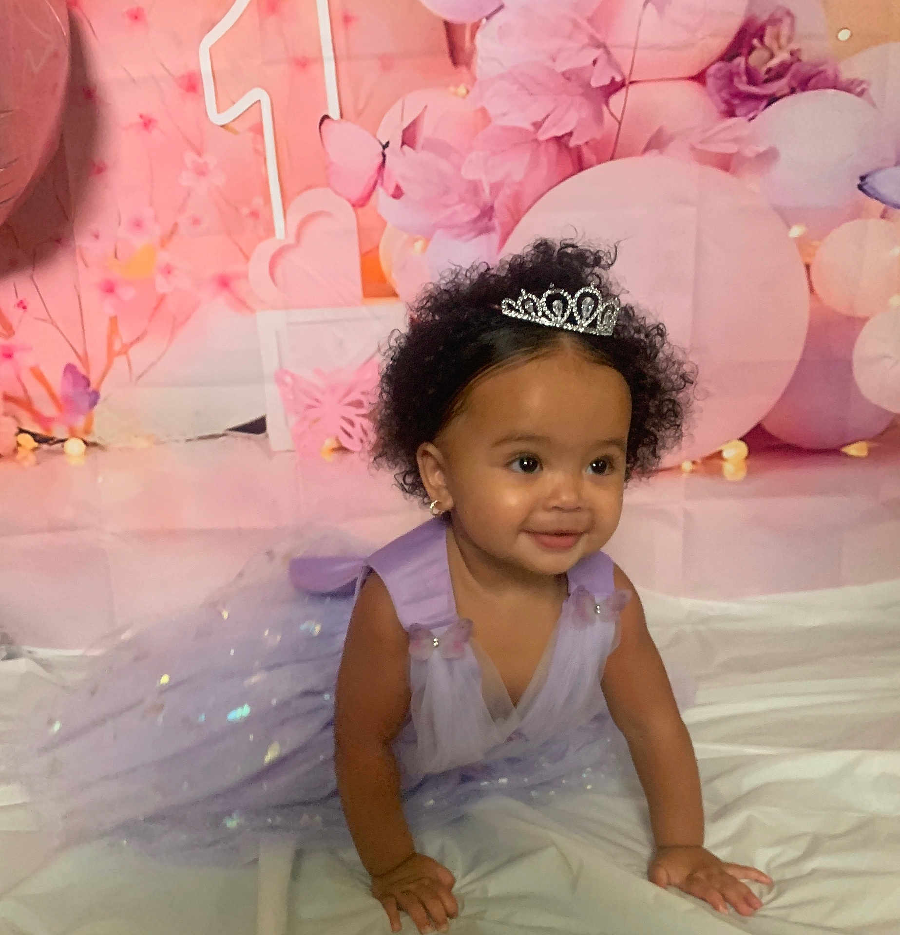 Ahnila is registered to the contest to win money with this photo: toddler, child, princess, tiara, dress, lavender, crawling, smiling, birthday, celebration, balloons, butterflies, pink, purple, curly_hair, earrings, white_sheet, background, happy, cute