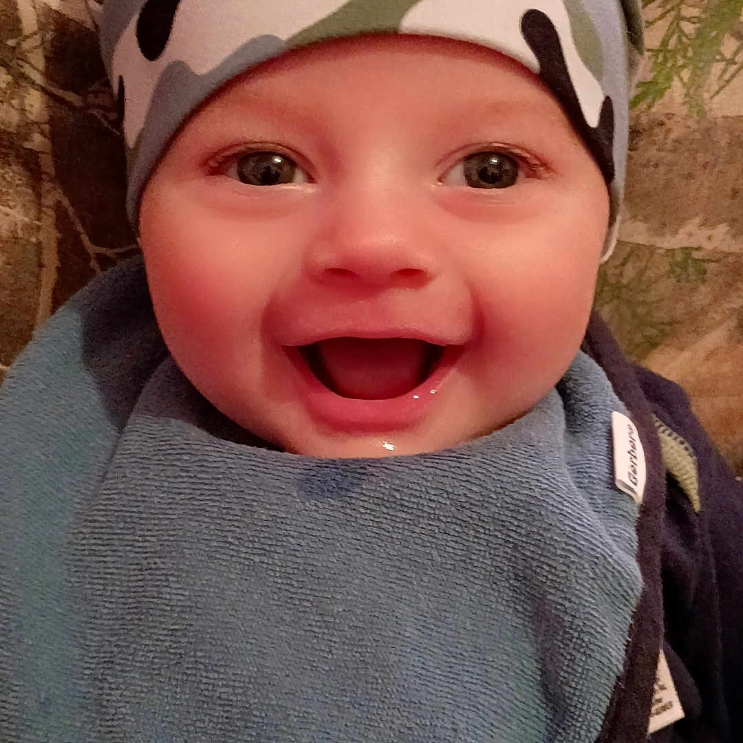 Milo joined the competition — help win amazing prizes! baby, smiling, face, hat, bib, camouflage, child, happy, indoor, person, portrait, cute, infant, clothing, closeup, young, headwear, babywear, sitting, expression