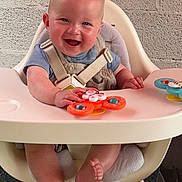 Gabin a rejoint le concours — aidez-le/la à gagner de superbes lots ! baby, high_chair, toy, smiling, happy, child, infant, blue_shirt, overalls, feet, hands, playful, indoor, seat_belt, wooden_legs, green_grass, gray_wall, cute, cheerful, portrait
