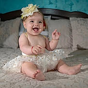 Sofia is registered to the contest to win money with this photo: baby, child, flower_headband, tutu, smiling, happy, sitting, bed, pillow, blanket, indoors, cute, infant, joyful, apparel, skin, foot, hand, headwear, portrait