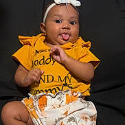 De'Lysia joined the competition — help win amazing prizes! baby, child, clothing, couch, cute, floral_shorts, footwear, happy, headband, indoor, infant, person, playful, portrait, sandals, sitting, smiling, tongue_out, white_bow, yellow_shirt
