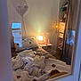 Nao a rejoint le concours — aidez-le/la à gagner de superbes lots ! cat, bed, blanket, pillow, lamp, nightstand, curtain, window, heart_light, flower_vase, bedroom, reflection, soft_lighting, decor, indoor, cozy, furniture, white_wall, stuffed_toy, relaxing
