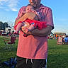baby, cap, casual_clothing, child, daylight, event, family, grass, holding, man, nature, outdoor, park, people, recreation, red_dress, relaxation, shorts, sky, summer