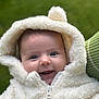 baby, child, smile, hoodie, white, fluffy, pom_pom, cute, portrait, outdoor, green_background, face, happy, warm_clothing, infant, person, close_up, eyes, skin, zipper
