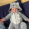 Elio participe au concours pour gagner de l'argent avec cette photo : baby, child, koala_onesie, gray_clothing, hooded_outfit, cushion, blue_background, indoor, infant, cute, portrait, childrens_fashion, soft_texture, seated, hands_visible, expression, cozy, casual, person, young