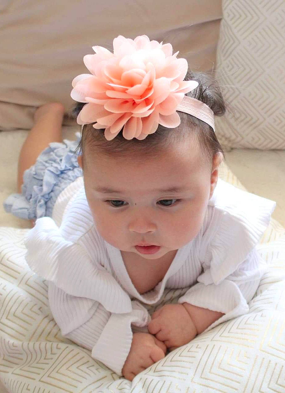Maïlys participe au concours pour gagner de l'argent avec cette photo : baby, baby_toddler_clothing, chin, comfort, dress, eyebrow, finger, flower, gesture, hair, hand, happy, head, headband, headgear, headpiece, person, petal, pink, plant