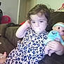 toddler, child, pacifier, doll, dress, curly_hair, couch, indoor, toy, brown_couch, patterned_dress, relaxed, young_child, furniture, home, person, cute, baby_doll, seated, casual