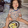 Elizabeth is registered to the contest to win money with this photo: bed, blanket, child, clothing, cozy, curly_hair, cute, eating, food, fork, happy, indoor, legs, meal, pacifier, pillow, plate, smiling, striped_shirt, toddler