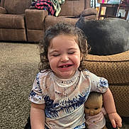 Elizabeth joined the competition — help win amazing prizes! carpet, child, clothing, couch, curly_hair, cute, doll, furniture, happy, home, indoor, laughing, living_room, person, seated, shorts, smiling, toddler, toy, tshirt