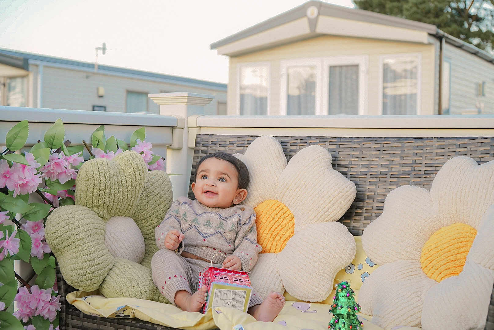 Myra joined the competition — help win amazing prizes! baby, child, smiling, plush_pillow, flower_pillow, wicker_bench, outdoor, toy_box, pink_flowers, green_leaves, knitted_clothing, happy, cute, infant, decor, cushion, sitting, garden, daylight, cozy