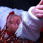 Amber joined the competition — help win amazing prizes! baby, infant, santa_hat, white_knitwear, hand, face, holiday, christmas, tinsel, festive, red, cozy, cute, sleepy, closeup, portrait, indoors, decoration, winter, holiday_season