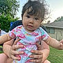 Arabelle joined the competition — help win amazing prizes! baby, child, person, outdoor, grass, tree, house, shirt, hands, face, curly_hair, sky, daylight, holding, sitting, casual_clothing, nature, yard, portrait, cute