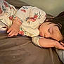 baby, sleeping, child, face, hand, onesie, floral_pattern, bed, pillow, blanket, indoors, cute, peaceful, rest, infant, soft_lighting, portrait, toddler, cozy, relaxation