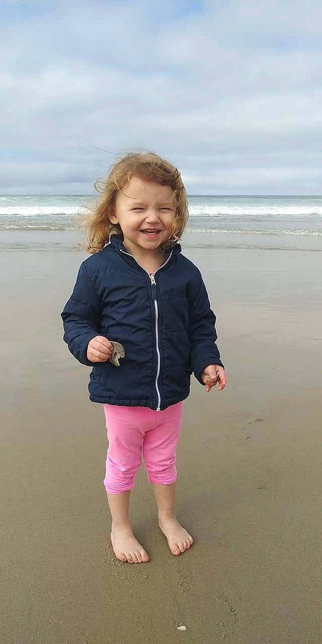 Jazmine is registered to the contest to win money with this photo: beach, child, jacket, joy, ocean, outerwear, person, pink, play, sea, sleeve, smile, standing, summer, toddler, vacation