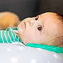 baby, infant, face, closeup, profile, lying_down, green_clothing, striped_clothing, pillow, teething_toy, soft_focus, curious_look, indoor, child, young_child, skin, head, eyes, portrait, resting