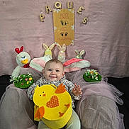 Romy participe au concours pour gagner de l'argent avec cette photo : baby, bunny_ears, easter, plush_toys, yellow_basket, chick, decorations, flowers, pink_fabric, cushion, chair, smiling, child, holiday, indoor, festive, cute, portrait, celebration, seated