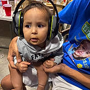 Axeill joined the competition — help win amazing prizes! toddler, headphones, child, person, indoor, table, cups, clothing, sitting, holding_hands, adult, floor, chair, hoodie, shorts, foot, hand, looking, expression, casual