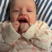 Amelia is registered to the contest to win money with this photo: baby, infant, pajamas, floral_pattern, hands, face, smiling, cushion, striped, blue_and_white, close_up, cute, child, sleepwear, young, indoors, soft_lighting, expressive, tiny_fingers, comfort