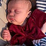 baby, sleeping, infant, maroon_clothing, bow, blanket, striped_blanket, floral_blanket, peaceful, face, hand, soft_lighting, indoors, cozy, cute, child, portrait, resting, small_hands, newborn