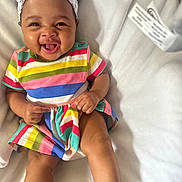 Ryleigh is registered to the contest to win money with this photo: baby, child, smiling, headband, colorful_clothing, striped_dress, happy, cute, infant, sitting, blanket, indoors, portrait, skin, face, hands, legs, footwear, bow, joyful