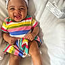 baby, child, smiling, headband, colorful_clothing, striped_dress, happy, cute, infant, sitting, blanket, indoors, portrait, skin, face, hands, legs, footwear, bow, joyful