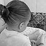 child, back_view, tied_hair, black_and_white, socks, shirt, sitting, cushion, patterned_tiles, floor, indoor, young_child, cute, hair_bun, feet, casual, relaxed, home, portrait_style, monochrome