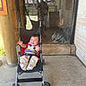 baby, child, stroller, smiling, outdoor, portrait, sitting, infant, colorful_clothing, striped_shirt, pants, shoes, reflection, glass_window, adult, porch, wooden_post, brick_wall, concrete, zoo