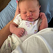 Braley is registered to the contest to win money with this photo: newborn, baby, sleeping, infant, portrait, face, floral_outfit, onesie, fist, hand, cradled, adult_arm, bed, blanket, pillow, indoors, close_up, peaceful, family, photography