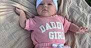 Braley is registered to the contest to win money with this photo: baby, infant, child, portrait, lying_down, outdoor, blanket, grass, pink_clothing, white_headband, bow, baby_girl, face, hands, arms, legs, text_on_clothing, fashion, natural_light, closeup