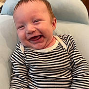Kane is registered to the contest to win money with this photo: baby, child, cushion, cute, expression, face, furniture, hand, happy, head, indoor, infant, joy, onesie, person, sitting, skin, smiling, striped_clothing, young