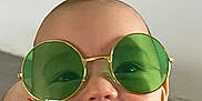 Henri participe au concours pour gagner de l'argent avec cette photo : accessory, baby, bib, cheeks, close_up, clothing, eyes, eyewear, face, green_sunglasses, grin, happy, head, indoor, infant, person, portrait, smile, sunglasses, wall