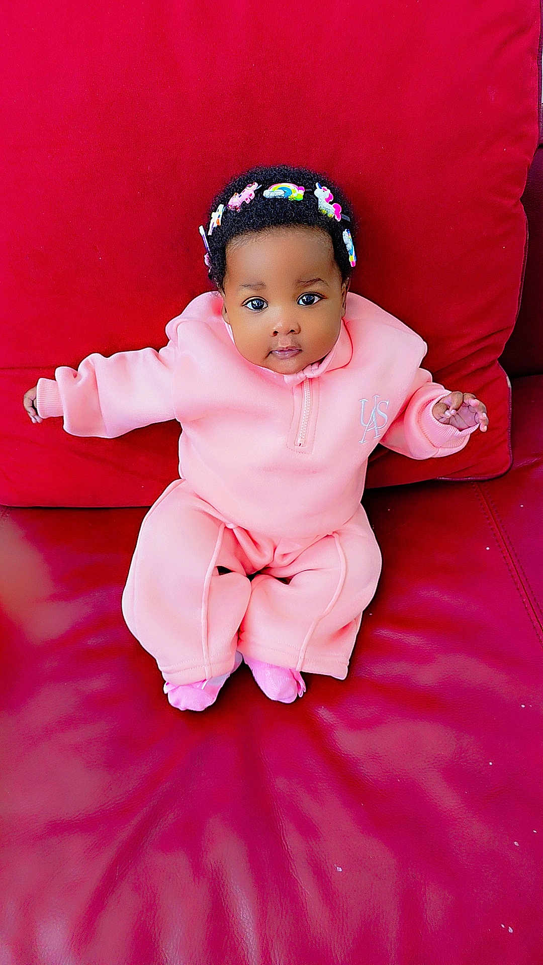 Ilerioluwa is registered to the contest to win money with this photo: baby, child, pink_clothing, headband, unicorn, rainbow, red_couch, leather, sitting, cute, infant, portrait, indoors, cozy, small_hands, looking_at_camera, adorable, bright_colors, young, comfortable