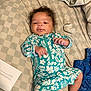Alani is registered to the contest to win money with this photo: baby, infant, bed, blanket, clothing, romper, curly_hair, sock, paper, text, blue_clothing, pattern, floral, hand, foot, face, person, laying_down, indoors, cozy