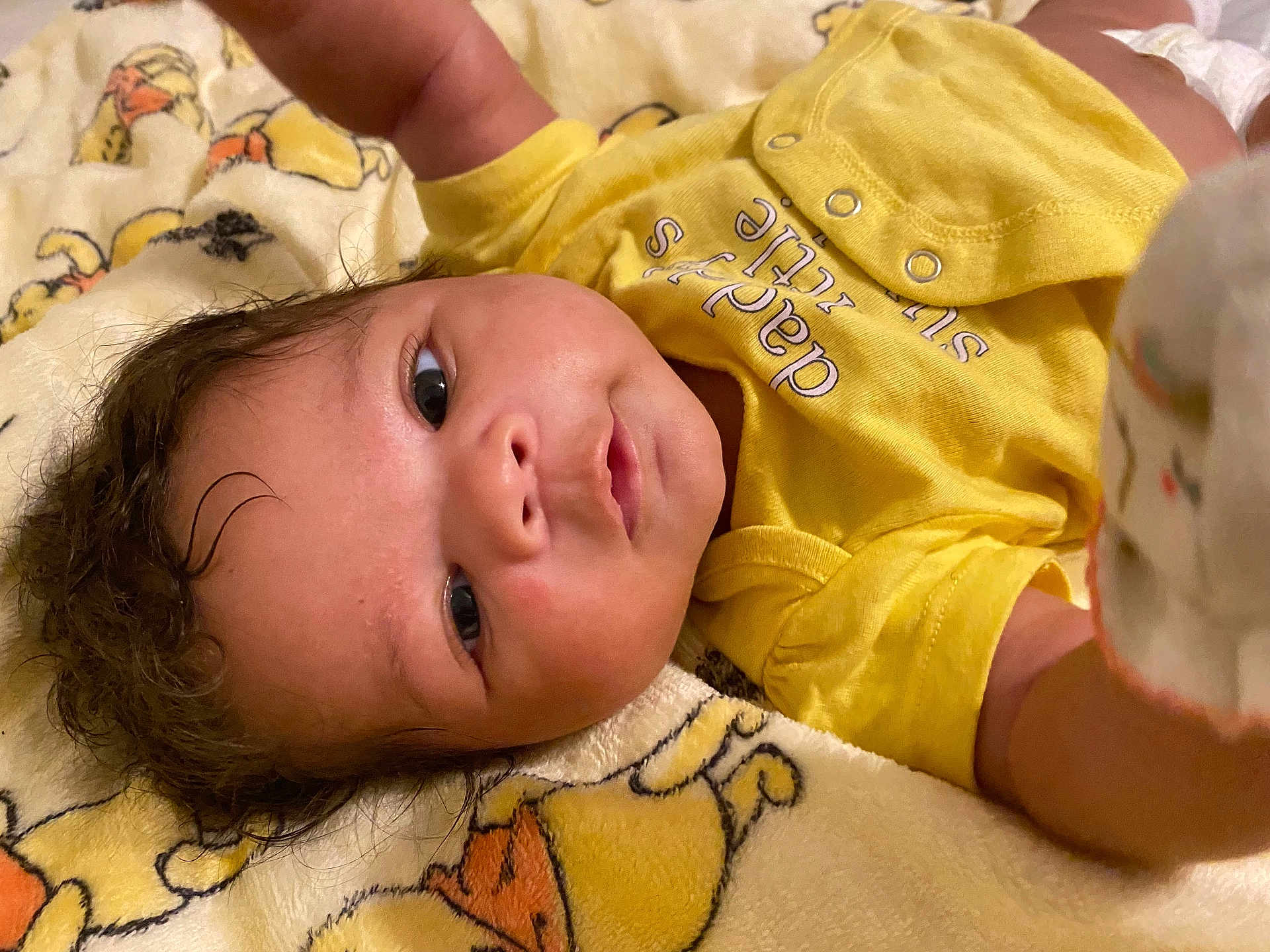 Alani is registered to the contest to win money with this photo: baby, infant, yellow_clothing, blanket, cartoon, face, head, skin, hair, expression, lying_down, cute, indoors, child, portrait, newborn, soft_texture, comfort, clothing, person
